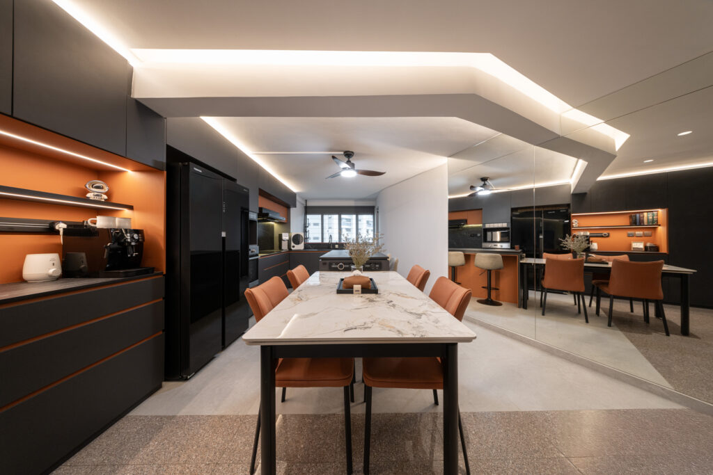 Full-height dark kitchen cabinets paired with warm orange recess accents.